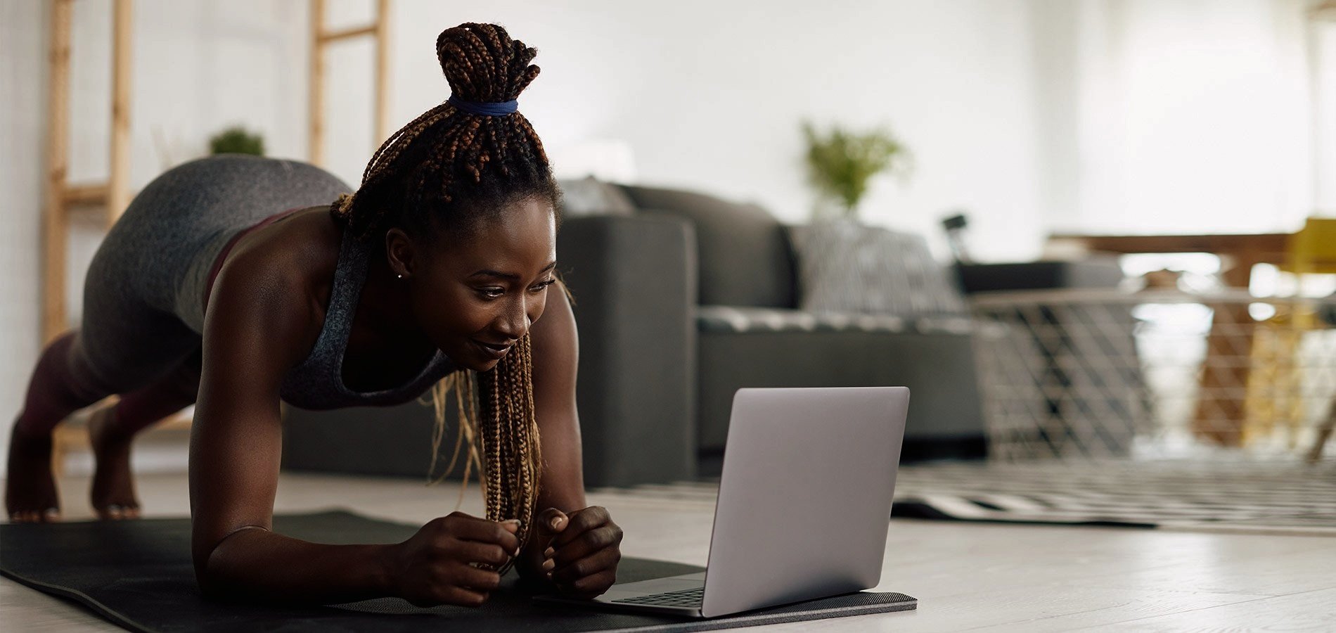 Woman performing a plank exercise at home while watching a laptop screen.