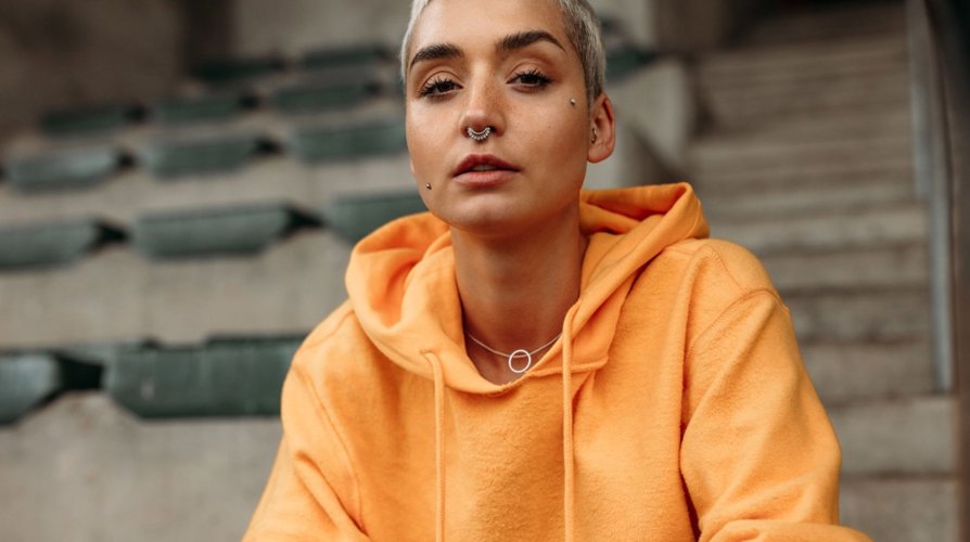 Girl wearing an orange hoodie standing against a neutral background with soft natural light.