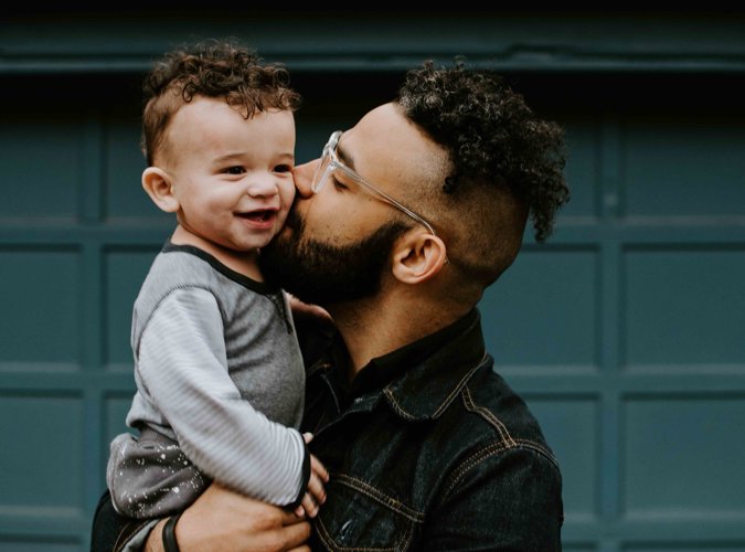 Man kneeling and kissing young son on the forehead in a family moment.