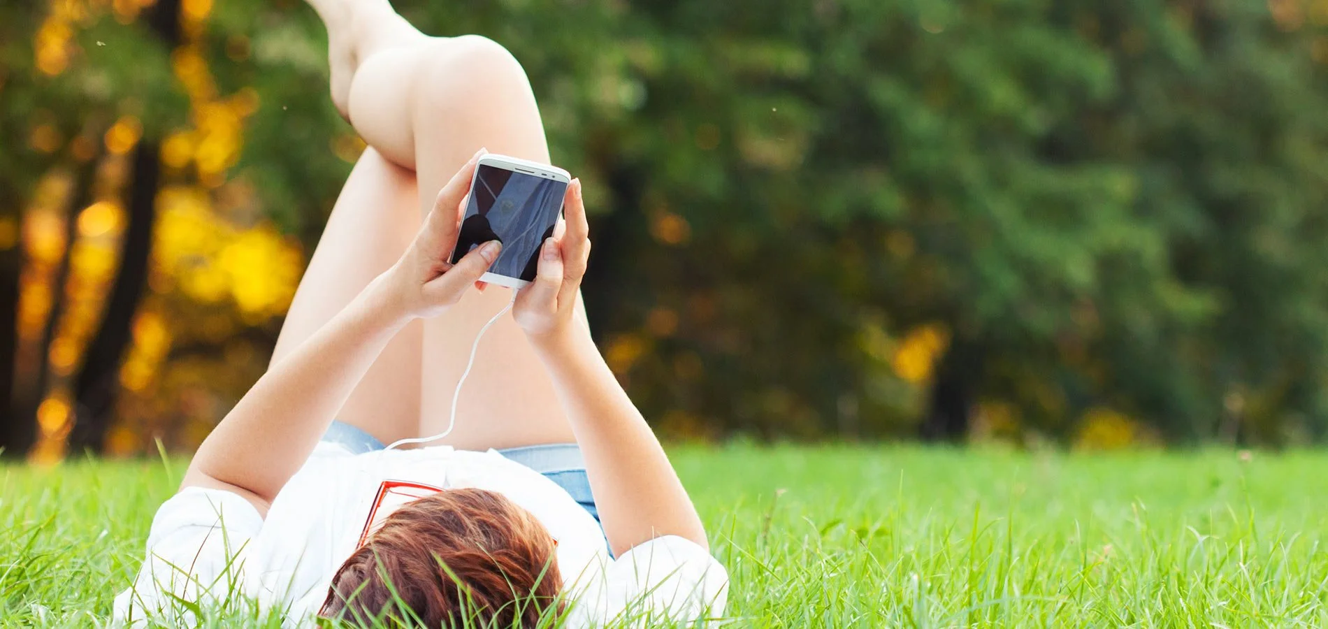 Woman lying in a park using her phone, enjoying outdoor relaxation