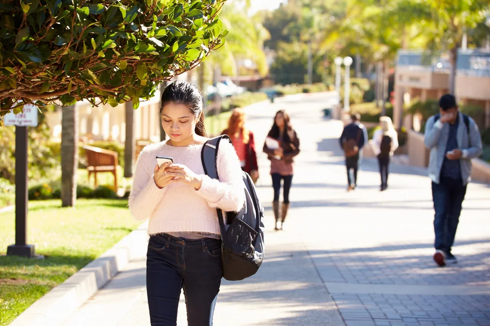 Student walking on a university campus while looking at her phone